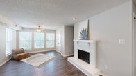 This single-floor residence at 2144 Village Green Pkwy in Chesterfield, Missouri offers a well-organized layout with a variety of functional living spaces. The living room serves as the centerpiece of the home, highlighted by a white brick fireplace with a clean mantel, dark hardwood-style flooring, and a ceiling fan. A bank of windows along one wall allows generous natural light to fill the room, creating a bright and welcoming atmosphere. A textured ceiling runs throughout the main living areas, adding a classic residential feel.

The kitchen is efficiently designed with white cabinetry, dark granite-style countertops, a peninsula with a sink, and black appliances including a refrigerator, range, and over-the-range microwave. The space flows openly toward the dining and living areas. Adjacent to the kitchen is an additional room featuring hardwood-style flooring, suitable for use as a dining area or flex space.

The bedrooms are carpeted for comfort, each equipped with ceiling fans and ample natural light from windows with blinds. The primary bedroom includes access to a walk-in closet and connects directly to a full bathroom. The bathroom features a tub-shower combination, dark countertops, and wood-style flooring. Throughout the home, neutral tones and clean finishes create a cohesive, move-in ready environment.