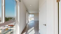 Located on Beverly Boulevard in Los Angeles, this modern 1-bedroom, 1-bathroom unit offers a thoughtfully designed open layout filled with abundant natural light. Light wood-tone flooring runs throughout, complementing the clean white walls and contemporary finishes that define the space.

The living area is expansive and airy, featuring large floor-to-ceiling windows and corner glass panels that frame sweeping panoramic views of the Los Angeles skyline and surrounding neighborhoods. Recessed lighting provides additional illumination throughout.

The kitchen is efficiently designed with white quartz countertops, light wood cabinetry, a subway tile backsplash, and stainless steel appliances including a gas range, over-the-range microwave, dishwasher, and full-size refrigerator.

The bedroom is comfortably sized, featuring large windows with elevated city views, light flooring, and direct access to a second, smaller adjacent room ideal for use as a home office or walk-in closet area.

The bathroom is clean and modern, featuring a subway-tiled tub and shower combination, a single-sink vanity, and light wood-style tile flooring. The overall design of the unit reflects a minimalist, contemporary aesthetic well-suited for urban living in the heart of Los Angeles.