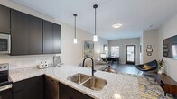 This well-appointed 1-bedroom, 1-bathroom unit at 316 Main St in Hamilton, Ohio offers a thoughtfully designed, open-concept floor plan. The combined kitchen and living area serves as the heart of the home, where the kitchen stands out with dark cabinetry, light granite countertops, a double undermount sink with a matte black faucet, and a full suite of stainless steel appliances including a refrigerator, range, microwave, and dishwasher. Elegant pendant lighting over the island and wood-look flooring throughout the main areas add to the modern aesthetic. The living room flows seamlessly toward a glass door entry, allowing natural light to fill the space, and offers room for both a seating and dining area. The bedroom features plush carpet, dual windows that bring in additional natural light, and a sliding double-door closet with a dark finish. The bathroom is outfitted with a granite-topped vanity with dark cabinetry, wood-look flooring, and a full tub-shower combination with tile surround. A dedicated laundry room with full-size washer and dryer, water heater, and electrical panel completes this efficient and modern living space.