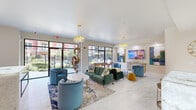 Located at 925 S Main St in Grapevine, TX, this thoughtfully designed single-floor communal space offers an open, airy layout that seamlessly integrates a living room, dining area, and fully equipped kitchen. Underfoot, large-format marble-look tile flooring flows throughout, lending a clean, upscale aesthetic to every area.

The living room is a vibrant gathering space anchored by a plush emerald green sofa, coordinating teal barrel chairs, and bold gold accents. Statement crystal and sculptural gold chandeliers hang overhead, complementing an array of colorful original artwork displayed on the walls. A wall-mounted flat-screen TV and a sleek linear fireplace add both function and ambiance. Floor-to-ceiling windows and glass doors flood the space with natural light and provide direct views of the landscaped outdoor patio.

A dedicated game area features a full-size billiards table, high-end pendant lighting, and additional seating, making it an ideal entertainment hub. Adjacent café-style tables with blue chairs offer a relaxed dining setting bathed in natural light from the surrounding windows.

The kitchen is a standout in elegance — outfitted with crisp white shaker cabinetry adorned with brushed gold hardware, a diamond-pattern tile backsplash, marble countertops, and a large waterfall-edge island with seating. Premium white and gold appliances complete this sophisticated culinary space.