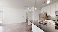 This single-story, one-bedroom, one-bathroom unit offers a thoughtfully designed layout with a consistent modern aesthetic throughout. Polished concrete floors extend across all living areas, providing a sleek, industrial character that unifies the space.

The open-concept living area features multiple windows and a glass-paned exterior door that invite abundant natural light, creating a bright and airy atmosphere. A ceiling fan adds both function and comfort to the main living zone.

The kitchen is well-appointed with white shaker-style cabinetry extending to the ceiling, dark granite countertops, a gray subway tile backsplash, and a full suite of stainless steel appliances, including a refrigerator, electric range, microwave, and dishwasher. A peninsula with an undermount sink provides additional prep and casual dining space.

The bedroom accommodates a comfortable layout, benefits from natural light via double windows, and includes a ceiling fan. A dedicated closet provides storage, and the room connects conveniently to the rest of the unit.

The bathroom features large-format white tile surrounding a soaking tub with an overhead shower, white cabinetry with brushed nickel hardware, a dark granite vanity top, and a vessel sink. A dedicated laundry room with washer and dryer hookups completes this efficiently organized unit.