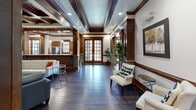 Located at 42 Senator Reynolds Rd in Woodfin, NC, this thoughtfully designed single-floor space blends craftsman-inspired architecture with warm, inviting interiors. Rich dark hardwood floors run throughout the main areas, complemented by striking dark wood coffered ceilings with decorative columns that lend the space a refined, upscale character.

The expansive living room serves as the heart of the space, anchored by a floor-to-ceiling stacked stone fireplace with a mounted flat-screen television and flanking built-in shelving. Comfortable seating arrangements invite gathering, while recessed lighting and ceiling fans enhance the welcoming ambiance. French doors with divided-light glass panes provide a natural focal point, allowing abundant natural light to filter in. A kitchenette area with a bar-height counter, cabinetry, and stainless steel appliances is conveniently accessible from the main living area.

A reception or waiting area near the entry features additional seating, pendant lighting, and warm wood millwork, creating a polished first impression. The dedicated office is equipped with a built-in desk, upper cabinetry, and granite-style countertops, accessed through a glass-paned door. A unique unclassified room features vaulted ceilings, soft flooring tiles, and minimal décor with an "inhale / exhale" wall accent, functioning as a tranquil meditation or wellness space.