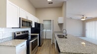 Located at 200 Village Blvd in Davenport, Florida, this single-floor residence offers a well-designed layout with modern finishes throughout. The kitchen is a standout feature, equipped with stainless steel appliances including an electric range, over-the-range microwave, and refrigerator. White shaker-style cabinetry, granite countertops, and a classic subway tile backsplash give the kitchen a clean, contemporary aesthetic. A peninsula with a double-basin sink adds additional prep and dining space. A dedicated in-unit laundry area is conveniently accessible directly from the kitchen. Wood-look flooring runs through the kitchen and wet areas, while plush carpeting extends through the living spaces and bedrooms, adding warmth and comfort. The living area is generously sized with large windows that invite natural light and a sliding glass door leading to an outdoor view. The bedrooms feature vaulted ceilings, ceiling fans, and ample natural light from well-placed windows. The bathrooms are finished with granite-topped vanities, white cabinetry, wood-look flooring, and full tub-shower combinations with brushed nickel hardware and safety grab bars, combining practicality with a refined look throughout.