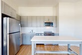 This three-bedroom, two-bathroom unit at 950 S George Mason Drive in Arlington, Virginia offers a well-designed single-floor layout with a clean, modern aesthetic throughout. Light wood-style flooring runs continuously across the living spaces, complementing the bright white walls and creating a warm, cohesive feel.

The open-concept kitchen and dining area serves as the heart of the unit, featuring gray shaker-style cabinetry, white subway tile backsplash, light-toned countertops, and a full suite of stainless steel appliances including a refrigerator, range, and over-the-range microwave. A central island with a white surface provides additional prep and dining space.

The three bedrooms are bright and airy, each benefiting from large windows that invite abundant natural light and offer views of the surrounding Arlington neighborhood and treeline. The primary bedroom provides a generous footprint with ample room for furnishings. Five closets are distributed throughout the unit, ensuring excellent storage capacity.

The two bathrooms are finished with large-format tile flooring, floating wood-tone vanities with dark countertops, illuminated mirrors, and clean white walls. One bathroom features a tub-shower combination with subway tile surround. An in-unit laundry area and a connecting hallway complete the thoughtfully organized floor plan.
