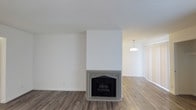 This single-floor, 2-bedroom, 2-bathroom residence offers a thoughtfully designed layout that balances comfort and functionality. The living area serves as the heart of the home, highlighted by a classically styled fireplace with ornate detailing and a substantial surround that draws the eye and anchors the room. Warm wood-style flooring flows throughout, adding a sense of continuity and warmth to the open space. Crisp white walls and smooth ceilings enhance the brightness of the interior, creating a clean and airy ambiance. A pendant light fixture is visible in the adjoining area, providing gentle, focused illumination that complements the natural light filtering through the windows. The open sightlines between the living and adjacent spaces contribute to an expansive feel, making the home appear generous and well-connected. The neutral color palette throughout provides a versatile backdrop suited to a variety of furnishing styles. This residence offers a welcoming atmosphere with timeless finishes and practical details that make it a functional and comfortable place to call home.