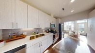 This well-designed 1-bedroom, 1-bathroom residence at 320 Revere offers a thoughtful single-floor layout that balances modern finishes with comfortable living. The kitchen is a standout feature, showcasing light wood-grain cabinetry extending to the ceiling for generous storage, crisp white quartz countertops, a stainless steel undermount sink, and a sleek subway tile backsplash. A full suite of stainless steel appliances—including a refrigerator, electric range, over-the-range microwave, and dishwasher—completes the space. The kitchen flows directly into the living area, which benefits from large windows and a glass door that fill the room with natural light and provide outdoor views, enhancing the open, airy ambiance. Warm hardwood flooring runs throughout the main living spaces. The bedroom is a calm, neutral retreat with plush carpeting and ample natural light. It connects directly to a dedicated closet area and the full bathroom, which features tile flooring, a well-lit vanity with white cabinetry, and a backlit mirror. The overall design aesthetic is clean and contemporary, with a warm, neutral palette that creates an inviting and cohesive atmosphere throughout the home.