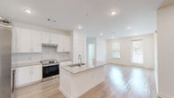Located in Kennesaw, GA, this well-designed 3-bedroom, 2-bathroom single-story home offers a bright, modern interior with a thoughtful open-concept layout. The kitchen and living area flow seamlessly together, anchored by a central island featuring a granite countertop with an undermount sink. White shaker cabinetry lines the kitchen walls, complemented by a classic tile backsplash and a full suite of stainless steel appliances, including a refrigerator with ice maker, range, and microwave. Light hardwood flooring runs throughout the main living areas, enhancing the clean, airy aesthetic. The living room receives natural light through large windows and a glass door that opens to the outdoors. The bedrooms are carpeted for comfort, each with neutral tones and ceiling fans. The primary bedroom includes a spacious walk-in closet with wrap-around wire shelving. The bathrooms are finished with granite-topped white vanities, large mirrors, and tiled shower enclosures. Recessed lighting throughout maintains a bright, polished atmosphere. The overall design is clean and contemporary, offering a move-in ready home with quality finishes at every turn.