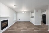 This single-floor residence offers a well-organized layout with a clean, modern aesthetic throughout. The living room serves as the heart of the home, featuring a built-in fireplace framed by a white mantel, wood-look plank flooring, and a sliding glass door with vertical blinds that opens to a private outdoor area, allowing natural light to fill the space. An additional window further brightens the room.

Adjacent to the living area, the dining space is defined by an elegant chandelier overhead and wood-look flooring that continues seamlessly from the living room. A pass-through opening connects the dining area directly to the kitchen, enhancing the open flow between spaces. The kitchen is well-appointed with white shaker-style cabinetry, subway tile backsplash, dark countertops, a stainless steel sink, and black appliances including a range, dishwasher, and refrigerator.

The bedrooms feature plush carpeting and neutral wall tones, with windows providing views of the surrounding greenery. Closet space is available in the living area as well. The bathroom is thoughtfully designed with accessibility in mind, equipped with grab bars near the tub and vanity area, wood-look flooring, a wide vanity with a vessel sink, and a full soaking tub.