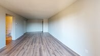 Located at 2091 Silver Bell Rd in Eagan, MN, this 2-bedroom, 1-bathroom unit offers a practical and well-organized single-floor layout. The living room is bright and open, featuring wood-style plank flooring, a textured ceiling, baseboard heating, and a wall-mounted AC unit. A sliding glass door leads to a private balcony with outdoor views, filling the space with natural light. Adjacent to the living area, the combined dining and kitchen space features a galley-style layout with warm wood cabinetry, dark countertops, a double sink, and white appliances including a refrigerator and range. Both bedrooms are carpeted and include ceiling fans, wall AC units, and baseboard heating. The primary bedroom offers generous proportions, while the second bedroom benefits from a large window with natural light. Four closets throughout the unit provide ample storage. The bathroom is finished with white tile surrounding a full soaking tub and shower combination. A hallway connects the main living areas to the bedrooms and bathroom, creating a cohesive and efficient floor plan suited for comfortable residential living.