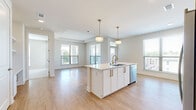 Located at 1003 Ridgewalk Pkwy in Woodstock, GA, this well-appointed single-floor residence offers a thoughtfully designed open-concept layout. The combined kitchen and living area serves as the heart of the home, anchored by a sleek central island with a undermount sink, gold-toned hardware, and pendant lighting overhead. The kitchen is outfitted with crisp white cabinetry, a decorative hexagonal tile backsplash, stainless steel appliances including a range, microwave, and refrigerator, and light wood-look flooring that extends seamlessly into the living space. Multiple windows flood the area with natural light and provide views of the surrounding Woodstock community. The bedroom is a comfortable retreat featuring a tray ceiling, plush carpeting, and large windows dressed with blinds that allow for adjustable light control. A private balcony door offers direct outdoor access, complemented by a ceiling fan for year-round comfort. A dedicated closet provides practical storage. The overall aesthetic is clean and contemporary, with a neutral color palette of whites and warm grays that lends the space a bright, airy ambiance throughout.