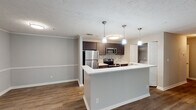 Located at 1073 McLendon Dr in Decatur, Georgia, this single-floor residence offers a well-designed layout with modern finishes and a cohesive neutral color palette throughout. The open-concept living and kitchen area serves as the heart of the home, where rich hardwood-style flooring extends seamlessly across the main living spaces. The kitchen is outfitted with dark espresso cabinetry, crisp white countertops, a mosaic tile backsplash, and a full suite of stainless steel appliances including a refrigerator, range, and built-in microwave. A peninsula with pendant lighting above provides additional prep space and casual seating. The living area is generously proportioned, featuring a ceiling fan and a large window that invites natural light and views of the surrounding greenery. The bedroom is carpeted for comfort and benefits from multiple windows and its own ceiling fan, creating a bright and airy retreat. The bathrooms are finished with dark vanity cabinetry, white countertops, and hardwood-style flooring, with one bathroom featuring a soaking tub and shower combination. An in-unit laundry area and ample closet space add to the overall practicality of this well-appointed residence.