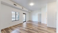 Located at 1120 S Walton Blvd in Bentonville, Arkansas, this modern single-floor unit offers a clean, contemporary design throughout. The open living area is anchored by warm wood-look plank flooring that extends seamlessly across the space, complemented by crisp white walls and a bright, airy atmosphere. Large windows fitted with blinds allow natural light to fill the room, while a glass door provides direct access to a private balcony with views of the surrounding community.

The kitchen is a standout feature, showcasing a two-tone design with white upper cabinetry and teal-accented lower cabinets, paired with white quartz countertops. Stainless steel appliances — including a refrigerator, electric range, over-the-range microwave, and dishwasher — complete this functional and stylish space.

A dedicated in-unit laundry nook houses a stacked washer and dryer, adding everyday convenience. The bathroom continues the teal cabinetry motif, featuring a white quartz vanity, a large mirror with overhead lighting, and tile flooring with white subway tile accents. The layout is efficiently organized, with multiple doorways connecting the living, sleeping, and utility areas in a logical and practical flow throughout the single-level floor plan.
