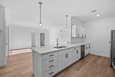 This single-floor unit showcases a clean, contemporary design throughout, highlighted by light hardwood flooring, white walls, and an abundance of natural light. The open-concept kitchen serves as a central feature, equipped with white shaker cabinetry, matte black hardware, light quartz countertops, and stainless steel appliances including an electric range, microwave, refrigerator, and dishwasher. A peninsula with an undermount sink extends into the living area, and two pendant lights hang above, adding a modern touch. The living area is bright and airy, benefiting from a sliding glass door that opens to a balcony offering outdoor views of the surrounding landscape. An in-unit laundry area with a washer and dryer is conveniently tucked nearby. The bedroom features plush carpeting, dual windows that invite generous natural light, and a double-door closet offering ample storage. The bathroom is finished with light hardwood-style flooring, a tub-shower combination, and a white vanity. Throughout the unit, the consistent use of neutral tones and modern finishes creates a cohesive, welcoming ambiance.