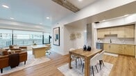 Located on Salt Lake City's historic South Temple Street, this thoughtfully designed 2-bedroom, 1-bathroom residence blends modern aesthetics with industrial-inspired architectural details. Light wood flooring flows throughout the open-concept main living area, where the kitchen, dining, and living spaces connect seamlessly. Exposed concrete columns and a reclaimed wood ceiling beam add character and texture to the otherwise clean, contemporary design.

The well-appointed kitchen features light wood cabinetry with gold-toned hardware, white quartz countertops, a tile backsplash, and a full suite of stainless steel appliances. The adjacent dining area comfortably accommodates a full dining table, while the living room benefits from wraparound floor-to-ceiling windows that flood the space with natural light and offer open outdoor views.

Both bedrooms are generously proportioned with plush carpet, large windows with exterior views, and access to a private balcony area. The primary bedroom includes an exposed concrete accent column and ceiling beam, reinforcing the space's industrial-modern character. The bathroom features warm wood vanity cabinetry with matching gold hardware, white countertops, and wood-look flooring. Recessed lighting throughout ensures a bright and inviting ambiance across every room.