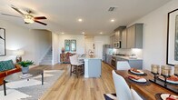 This two-story home offers a thoughtfully designed layout spread across two floors. The main level features an open-concept living, dining, and kitchen area finished with warm hardwood-style flooring throughout. The kitchen is equipped with stainless steel appliances, gray shaker-style cabinetry, granite countertops, and a central island with seating — ideal for both cooking and casual entertaining. The adjacent dining area benefits from natural light through large windows dressed with elegant curtains, while the living room offers a welcoming atmosphere with ceiling fan and defined sitting areas. A conveniently located half-bath powder room with a pedestal sink completes the ground floor. Upstairs, the primary bedroom is a spacious retreat featuring soft carpeting, a serene light-blue accent wall, ceiling fan, and access to a walk-in closet. Two additional bedrooms share a well-appointed full bathroom with a tub-shower combo and gray vanity cabinetry. A hallway connects all upper-level rooms with ease. Throughout the home, neutral tones, recessed lighting, and clean architectural lines create a cohesive and inviting ambiance suited for comfortable everyday living.