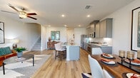 This two-story home offers a thoughtfully designed layout spread across two floors. The main level features an open-concept living, dining, and kitchen area finished with warm hardwood-style flooring throughout. The kitchen is equipped with stainless steel appliances, gray shaker-style cabinetry, granite countertops, and a central island with seating — ideal for both cooking and casual entertaining. The adjacent dining area benefits from natural light through large windows dressed with elegant curtains, while the living room offers a welcoming atmosphere with ceiling fan and defined sitting areas. A conveniently located half-bath powder room with a pedestal sink completes the ground floor. Upstairs, the primary bedroom is a spacious retreat featuring soft carpeting, a serene light-blue accent wall, ceiling fan, and access to a walk-in closet. Two additional bedrooms share a well-appointed full bathroom with a tub-shower combo and gray vanity cabinetry. A hallway connects all upper-level rooms with ease. Throughout the home, neutral tones, recessed lighting, and clean architectural lines create a cohesive and inviting ambiance suited for comfortable everyday living.