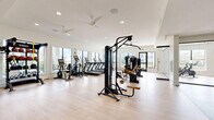 Located at 5201 W Hillsboro Blvd in Coconut Creek, FL, this well-appointed fitness center offers a comprehensive workout facility across a single floor. The space is divided into two distinct areas: a spacious main gym and a dedicated studio room, together providing a well-rounded fitness environment.

The main gym is bright and open, featuring light hardwood-style flooring and white walls that contribute to a clean, modern aesthetic. Large windows line the perimeter, flooding the space with natural light and offering views of the surrounding outdoor areas. Ceiling fans are installed throughout to maintain airflow and comfort. The room is comprehensively equipped with cardio machines including treadmills, ellipticals, and stationary bikes, alongside a robust selection of strength equipment such as cable machines, a functional trainer, free weights, and a TRX suspension system. Full-length mirrors enhance the sense of space and support proper form during workouts.

The adjacent studio room offers a quieter, more focused environment ideal for cycling and stretching. It features Peloton-style spin bikes, exercise mats, a wall-mounted television, and large windows with outdoor views. Ceiling fans and recessed lighting complete the comfortable, distraction-free setting. Together, the two rooms provide a versatile fitness facility suited for a wide range of workout routines.