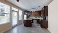 This single-floor space offers a thoughtfully designed open layout anchored by a standout kitchen. Rich, dark espresso cabinetry reaches toward the ceiling, providing generous storage while contrasting beautifully against the granite countertops and mosaic tile backsplash. A central kitchen island with matching granite extends the prep and dining surface, while stainless steel appliances — including a refrigerator, range, microwave, and dishwasher — complete the contemporary look. Track lighting illuminates the kitchen workspace, complementing the natural light that pours in through large windows fitted with blinds.

Polished concrete floors extend seamlessly throughout the entire unit, lending an industrial-modern aesthetic that ties each area together. The living area is open and adaptable, featuring a ceiling fan with light fixture overhead and neutral wall tones that create a bright, inviting atmosphere.

The bathroom is clean and functional, featuring full-height white subway tile surrounding a soaking tub and shower combination, paired with a toilet and vanity. The consistent use of neutral tones and quality finishes throughout the space reflects a cohesive design sensibility, making this unit a practical yet stylish place to call home.