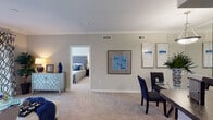 This single-story residence offers a thoughtfully designed layout that balances comfort and functionality. The open-plan living and dining area is finished with plush wall-to-wall carpeting and neutral gray walls adorned with crown molding, creating a clean, cohesive aesthetic. Large sliding glass doors in the living room invite natural light and provide access to an outdoor space, while decorative framed artwork adds visual interest throughout.

The galley-style kitchen features warm honey-toned cabinetry, dark granite-look countertops, a double stainless steel sink, and white appliances including a refrigerator and electric range. Wood-style flooring grounds the kitchen, which opens to the main living area via a breakfast bar pass-through.

The bedroom is a bright, inviting retreat highlighted by a bay window arrangement that floods the room with natural light and offers views of the surrounding greenery. Soft carpeting and a ceiling fan complete the comfortable atmosphere.

The full bathroom connects directly to the bedroom and includes warm wood-toned cabinetry, an extended vanity with generous counter space, a large mirror, and a shower-tub combination. The entryway provides a welcoming transition into the home, with tile flooring and a coat closet for added convenience.