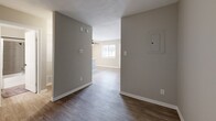 Located at 1610 E McKinney St in Denton, Texas, this efficiently laid-out single-floor unit offers a thoughtfully designed interior that maximizes its compact footprint. The open-concept living and kitchen area forms the heart of the space, where warm hardwood-style flooring extends seamlessly throughout. A ceiling fan in the living area promotes airflow and comfort, while a large window invites natural light, creating a bright and welcoming atmosphere.

The kitchen is a standout feature, showcasing a white peninsula countertop that provides additional workspace and a casual dining or prep area. White shaker-style cabinetry, a stainless steel refrigerator, a range with overhead ventilation, and a single-basin sink with a modern matte black faucet complete the well-appointed setup. The clean, neutral color palette of soft whites and warm grays lends the kitchen a fresh, contemporary feel.

The full bathroom is designed with practicality and style in mind, featuring a white vanity with ample cabinet storage, matte black hardware accents, a wall-mounted medicine cabinet with mirror, and a tub-shower combination finished with tasteful gray subway tile. A small window provides natural ventilation.

A hallway with a visible electrical panel connects the main living areas, offering a logical and functional flow throughout the home.