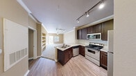 This well-appointed one-bedroom, two-bathroom residence offers a thoughtfully designed single-floor layout that maximizes functionality and comfort. The open-concept kitchen serves as the heart of the home, showcasing rich dark-wood cabinetry, light granite countertops, a tiled backsplash, and a full suite of stainless steel appliances including a range, microwave, dishwasher, and refrigerator. Track lighting illuminates the space, while a peninsula with a sink provides both prep space and a natural transition into the living area. Crown molding adds a refined architectural touch throughout.

The living room features plush carpeting, a ceiling fan, and a built-in shelving nook — ideal for display or storage — along with a window that invites natural light. The spacious primary bedroom is carpeted and includes a ceiling fan, with a dedicated walk-in closet outfitted with multi-tier wire shelving for organized storage. The primary bathroom impresses with a dual-sink vanity, granite countertops, dark cabinetry, wood-look flooring, and a walk-in shower. A second full bathroom provides added convenience for guests. Completing the home is a dedicated laundry room with side-by-side washer and dryer units.