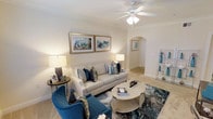 This single-story Dallas property showcases a thoughtfully designed living area that balances comfort and refined style. The living room serves as the centerpiece of the space, featuring warm neutral walls accented by crisp crown molding that frames the room with a clean, classic finish. A ceiling fan with an integrated light fixture anchors the ceiling, providing both function and a subtle decorative touch.

The flooring transitions between plush carpet in the living area and what appears to be light-toned tile beyond the arched doorway, adding visual variety and dimension. The arched passageway is a notable architectural detail, lending a soft, elegant character to the layout and connecting the living area to the adjoining spaces seamlessly.

Natural and ambient lighting work together to create a warm, inviting atmosphere throughout. The room is well-proportioned, offering comfortable seating arrangements with ample space to move. Neutral walls provide a versatile backdrop that complements the blue and cream furnishings visible in the space.

Overall, this Dallas property presents a welcoming, well-appointed interior with timeless architectural details and a cohesive, calming aesthetic.