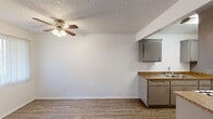 Located at 10453 Artesia Blvd in Bellflower, CA, this 2-bedroom, 1-bathroom single-story home offers a practical and comfortable layout. The combined kitchen and living area forms the heart of the home, featuring wood-style plank flooring, a ceiling fan with light fixture, and a textured ceiling. The kitchen is equipped with gray cabinetry, granite-style countertops, a double stainless steel sink, and a gas range, and opens directly into the living space for a connected, functional flow. A large window in the living area allows natural light to filter in and provides views of the surrounding greenery outside. The two bedrooms are carpeted and well-proportioned, with the primary bedroom offering generous space. Both bedrooms feature vertical blind-covered windows and closet access, with three closets distributed throughout the home for ample storage. A hallway connects the private areas of the home. The full bathroom includes a tub/shower combination, toilet, and vanity, finished with wood-style flooring and clean white walls. The overall aesthetic is clean and neutral, with white walls throughout creating a bright, move-in ready environment well-suited for comfortable everyday living.