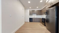 This thoughtfully designed one-bedroom, one-bathroom unit offers a modern living experience with consistent light wood flooring and crisp white walls throughout. The kitchen is a standout feature, equipped with warm wood-toned cabinetry, marble-look countertops, a full suite of black appliances including a range, refrigerator, and dishwasher, and recessed lighting that creates a bright, functional workspace. The open layout connects the kitchen seamlessly to the living area, which benefits from natural light via a window with blinds. Two hallways provide efficient transitions between rooms, contributing to a practical and well-organized floor plan. The bedroom is a cozy, light-filled retreat with a window that invites natural light and maintains a clean, neutral palette. The bathroom mirrors the design language of the rest of the unit, featuring a wood-finish vanity with a marble-look countertop, a large mirror, and a full soaking tub with a shower. Clean lines, neutral tones, and consistent modern finishes give the entire unit a cohesive and contemporary ambiance, making it a comfortable and stylish single-floor living space.