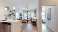 Located at 8500 Hunters Village Rd in Tampa, FL, this single-floor residence offers a thoughtfully designed open-concept layout that seamlessly connects the kitchen, dining, and living areas. The kitchen is outfitted with rich, warm-toned cabinetry extending to the ceiling, stainless steel appliances including a French door refrigerator, a gas range, and microwave, complemented by white quartz countertops and a breakfast bar with seating — ideal for casual dining or entertaining. Light wood-style flooring flows throughout the main living areas, adding warmth and continuity.

The living room is bright and welcoming, featuring large windows with wood blinds and patterned drapes that allow generous natural light while offering privacy. Ceiling fans are present in the main living area and bedrooms for added comfort.

The space includes multiple bedrooms, each well-lit with windows and ceiling fans. One bedroom features a soft, neutral palette with natural textures, while another is styled with a coastal-inspired teal and blue color scheme. Both rooms offer a tranquil retreat. The bathroom showcases a rich wood-toned vanity with white countertops and a large mirror. Throughout, the residence maintains a cohesive, contemporary aesthetic with coastal-inspired accents and curated décor.