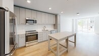 Located at 3348 W Moore St in Richmond, Virginia, this two-story home offers a clean, contemporary design defined by an all-white palette, light hardwood flooring, and an abundance of natural light throughout. The main level opens into a generous living area with large floor-to-ceiling windows that invite street views and sunlight, creating an airy, open atmosphere. The modern kitchen is well-appointed with gray shaker-style cabinetry extending to the ceiling, white subway tile backsplash, stainless steel appliances including a range, microwave, refrigerator, and dishwasher, complemented by gold-accented hardware and a central island for additional workspace and seating. A dedicated half bath on the main level features matching hardwood flooring and gold fixture details. The upper level houses the bedrooms, each with closets and access to well-designed bathrooms. One bathroom offers a tiled tub-shower combo with subway tile surround, while a second features a frameless glass walk-in shower with matching tile work. Throughout both floors, the consistent use of white walls, recessed lighting, and light wood flooring creates a cohesive, modern aesthetic. A wood-railed staircase connects the two levels, completing this thoughtfully designed Richmond home.