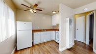 This single-floor residence in Livermore, California offers a clean, functional layout with a cohesive design throughout. The kitchen is efficiently arranged in an L-shape, outfitted with white cabinetry, warm wood-toned countertops, a tile backsplash, and white appliances including a full-size refrigerator and range. Wood-look vinyl flooring extends through the kitchen and main living areas, providing durability and a warm aesthetic. A ceiling fan with light fixture overhead adds both comfort and utility to the kitchen space, while a wall-mounted heater ensures year-round climate control. The living area features a large window fitted with vertical blinds, allowing natural light to filter in while maintaining privacy. An arched entry door adds a subtle architectural detail to the entryway. The bedroom is generously proportioned, finished with plush carpeting, a ceiling fan, and a window with vertical blinds. A built-in closet with shelving provides ample storage. An additional room features wood-look flooring bathed in natural light streaming through slatted blinds. The bathroom includes a full tub-shower combination with a tiled surround, wood-look flooring, and a window for natural ventilation. Neutral wall tones throughout lend the space a clean, move-in-ready appeal.