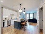 Located at 1134 Chambers Rd in Columbus, Ohio, this well-appointed 2-bedroom, 3-bathroom residence offers a thoughtfully designed single-floor layout. The open-concept kitchen and living area serves as the heart of the home, featuring white shaker cabinetry, a subway tile backsplash, stainless steel appliances, and a striking center island with a contrasting navy or blue painted base and granite countertop. Globe pendant lights hang above the island, adding a modern touch. Light hardwood flooring runs throughout the main living area, which flows seamlessly into the living room. The living room benefits from abundant natural light through large windows and a glass-panel door that opens to an outdoor balcony, providing views of the surrounding neighborhood. The primary bedroom is a comfortable retreat with soft carpet, built-in shelving, and generous natural light. The bathrooms are finished with large-format marble-style porcelain tile flooring and granite-topped vanities, lending a clean, upscale aesthetic. Each bedroom is served by its own dedicated closet with built-in shelving and hanging rods. The overall design balances modern finishes with a warm, livable ambiance throughout.