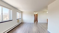This well-organized 2-bedroom, 1-bathroom single-floor unit offers a practical and comfortable layout designed for everyday living. The combined kitchen and living room forms the heart of the unit, featuring warm wood-look laminate flooring, a ceiling fan, and an open layout that encourages easy flow between cooking and living spaces. The galley-style kitchen is equipped with warm-toned wood cabinetry, white appliances including an electric range and refrigerator, light countertops, and a stainless steel sink — providing ample storage and workspace. A hallway connects the main living area to the private quarters, and includes a dedicated closet with louvered doors and built-in shelving, offering generous storage capacity. Both bedrooms are finished with soft carpeting and feature warm-toned wood doors. The primary bedroom is notably spacious and includes a wide bi-fold closet with built-in hanging rods and shelving. The second bedroom is comfortably sized and equally well-lit. The bathroom features a full tub and shower combination with clean white tile surround. Throughout the unit, neutral white walls and consistent flooring choices create a cohesive and clean aesthetic that is easy to personalize.