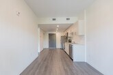 Located at 387 King Street East in Kitchener, Ontario, this compact and efficiently designed one-bedroom, one-bathroom unit offers a thoughtful modern layout with clean finishes throughout. The open-concept living and kitchen area is anchored by warm grey laminate flooring that runs continuously through the space, creating a cohesive and airy feel. A sliding glass door at the end of the living area provides access to a balcony and fills the room with natural light.

The kitchen is well-appointed with stainless steel appliances, including an electric range, over-the-range microwave, refrigerator, and dishwasher. Crisp white cabinetry with sleek bar-pull hardware lines the walls, complemented by light countertops and a stainless steel sink — offering ample storage and prep space for the footprint.

The bedroom is a bright, quietly composed room featuring a large black-framed window with green outdoor views and a full mirrored sliding-door closet that enhances the sense of space. Neutral white walls and consistent flooring maintain the unit's clean aesthetic.

The bathroom includes a soaker tub and shower combination, toilet, and vanity, finished in a simple, functional white palette. Throughout the unit, recessed and flush-mounted lighting provides practical illumination, while the overall design prioritizes clean lines and modern simplicity.