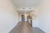 Located at 387 King Street East in Kitchener, Ontario, this compact and efficiently designed one-bedroom, one-bathroom unit offers a thoughtful modern layout with clean finishes throughout. The open-concept living and kitchen area is anchored by warm grey laminate flooring that runs continuously through the space, creating a cohesive and airy feel. A sliding glass door at the end of the living area provides access to a balcony and fills the room with natural light.

The kitchen is well-appointed with stainless steel appliances, including an electric range, over-the-range microwave, refrigerator, and dishwasher. Crisp white cabinetry with sleek bar-pull hardware lines the walls, complemented by light countertops and a stainless steel sink — offering ample storage and prep space for the footprint.

The bedroom is a bright, quietly composed room featuring a large black-framed window with green outdoor views and a full mirrored sliding-door closet that enhances the sense of space. Neutral white walls and consistent flooring maintain the unit's clean aesthetic.

The bathroom includes a soaker tub and shower combination, toilet, and vanity, finished in a simple, functional white palette. Throughout the unit, recessed and flush-mounted lighting provides practical illumination, while the overall design prioritizes clean lines and modern simplicity.