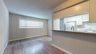 Located on Audley Street in Houston, TX, this single-story unit offers a well-organized layout with a clean, modern aesthetic throughout. The living area is bright and open, featuring light wood-tone laminate flooring, neutral gray walls, and a textured ceiling. A wide horizontal window allows natural light to fill the space, creating an airy feel. The flooring runs consistently through the main living and bedroom areas, contributing to a cohesive visual flow.

The kitchen is designed with a pass-through peninsula that connects it to the living area, topped with a dark granite-style counter that provides both workspace and a casual bar seating option. White cabinetry lines the kitchen walls with additional upper cabinetry above the pass-through, maximizing storage. The kitchen is equipped with white appliances, including a refrigerator and range, complemented by a subway tile backsplash and an undermount sink with a brushed nickel faucet.

The bedroom is a well-proportioned space with the same wood-tone flooring and includes a dedicated closet with built-in shelving. The bathroom features a full tub-shower combination with floor-to-ceiling wood-grain ceramic tile, accented by a mosaic tile inlay border, chrome fixtures, and a clean white basin and toilet.