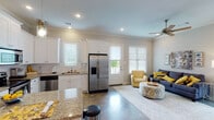 This single-story residence offers a thoughtfully designed open-concept layout that seamlessly connects the kitchen, dining area, and living room. The polished concrete floors throughout the main living spaces lend a contemporary, low-maintenance aesthetic, while crown molding adds a refined architectural detail to each room.

The kitchen is equipped with white shaker-style cabinetry, granite countertops, a subway tile backsplash, and a full suite of stainless steel appliances, including a French door refrigerator, electric range with over-the-range microwave, and dishwasher. A peninsula provides additional prep space and casual seating. The adjacent dining area accommodates a small table beneath elegant pendant and chandelier lighting.

The living room receives natural light through multiple windows fitted with white blinds and benefits from a ceiling fan overhead. A private entry door opens directly from this space to the exterior.

Both bedrooms feature carpet flooring, crown molding, ceiling fans, and neutral wall tones. The primary bathroom includes a walk-in tiled shower, granite vanity, and white cabinetry. The second bathroom offers a tub-shower combination with ample overhead storage.