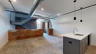 Located at 356 Hertel Ave, this one-bedroom, two-bathroom industrial loft blends raw architectural character with contemporary design across three thoughtfully laid-out floors. The main living level serves as the heart of the home, offering an open-concept dining, kitchen, and living area defined by polished concrete floors, exposed brick accent walls, and prominent silver ductwork running overhead — a hallmark of the loft's industrial aesthetic. The kitchen features a bold navy island with a white quartz countertop, stainless steel double sink, pendant lighting, white cabinetry, and subway tile backsplash. A steel staircase with cable railings connects the floors, adding to the industrial-modern character. The upper floor houses the generously sized primary bedroom, which benefits from soaring ceilings and an abundance of natural light. A sleek frosted-glass sliding partition adds a stylish room divider element. Both bathrooms are finished in a clean, modern style — one featuring white subway tile, a glass-enclosed shower, and concrete floors, while the other offers a backlit vanity mirror and stone tile flooring. Additional conveniences include a dedicated laundry area, entrance, closet, and multiple staircase connections throughout the multi-level layout.