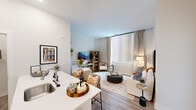 Located at 1112 First St in the heart of Old Town Alexandria, VA, this thoughtfully designed one-bedroom, one-bathroom residence offers a modern and efficient layout across a single floor. The open-concept kitchen and living area creates a seamless flow, anchored by a well-appointed kitchen featuring tall white shaker cabinets, quartz countertops with an undermount sink, a subway tile backsplash, and a full suite of stainless steel appliances including a French door refrigerator, electric range, and built-in microwave. A peninsula provides additional prep space and serves as a natural divider between the kitchen and living area. The living room is bathed in natural light through a large floor-to-ceiling window dressed with vertical blinds and drape panels, complemented by light wood-style flooring throughout. The bedroom offers a comfortable, carpeted retreat with a ceiling fan, generous closet space, and its own large window overlooking the exterior. The bathroom features a sleek, floor-to-ceiling tiled walk-in shower enclosed by sliding glass doors and paired with white cabinetry for ample storage. A dedicated laundry area with wire shelving adds everyday convenience. Clean white walls and recessed lighting throughout lend the space a bright, contemporary ambiance.