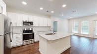 This well-appointed single-floor residence showcases a thoughtful layout with modern finishes throughout. The heart of the home is an open-concept kitchen that flows seamlessly into the living area. The kitchen is outfitted with crisp white cabinetry, a classic subway tile backsplash, stainless steel appliances including a range, microwave, and refrigerator, and a central island topped with granite countertops and an undermount sink. Rich hardwood-style flooring extends throughout the main living areas, complemented by recessed lighting that creates a bright, welcoming atmosphere. Large windows invite ample natural light into the living space, which also features a private entry door. The bedrooms are finished with plush carpeting, and one features a stylish sliding barn door leading to a walk-in closet with built-in shelving, while another offers a ceiling fan and multiple windows with outdoor views. The primary bathroom impresses with a dual-sink granite vanity, a large framed mirror, and a separate glass-enclosed walk-in shower. A secondary bathroom provides a full tub-shower combo with clean white tile surround and hardwood-style flooring. The overall design is clean, contemporary, and move-in ready.