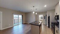 Located at 2112 Sherwood Ave in Holland, Michigan, this single-floor unit offers a well-designed, open-concept layout that maximizes both functionality and comfort. The kitchen serves as the centerpiece of the main living area, anchored by a large island with a dark countertop, double stainless steel sink, and pendant lighting overhead. White cabinetry provides ample storage, while black appliances — including a refrigerator, range, and over-the-range microwave — complete the space. The kitchen flows seamlessly into the living area, which features durable wood-look flooring throughout and neutral-toned walls that create a clean, versatile backdrop. Sliding glass doors in the living area open to a private balcony, offering views of the surrounding landscape and filling the space with natural light. The bedroom is generously sized, finished with plush carpeting and a window with blinds that frame outdoor views. A full bathroom includes a single-sink vanity with a white countertop, a mirrored medicine cabinet, and a tub-shower combination. An in-unit laundry area, accessible via a dedicated door off the kitchen, adds everyday convenience to this thoughtfully appointed space.