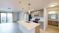 Located at 202 S Pinckney St in the heart of downtown Madison, Wisconsin, this modern one-bedroom, two-bathroom unit offers a well-designed single-floor layout with clean contemporary finishes throughout. The open-concept kitchen and living area serves as the centerpiece of the home, featuring a large quartz-topped island with an undermount sink and pendant lighting, light wood cabinetry, a subway tile backsplash, and a full suite of stainless steel appliances. Light wood-tone flooring runs through the kitchen and living areas, creating a warm, cohesive aesthetic. The living area is bright and open, with access to a private balcony through sliding glass doors that frame views of the surrounding Madison cityscape. A distinctive concrete column and ceiling fan add architectural character to the space. The primary bedroom is a comfortable size, also accessing the balcony via sliding doors and offering urban views. It features built-in closet shelving and connects to a dedicated bathroom. Both bathrooms are finished with clean white tile, light wood-tone flooring, dark-wood vanities, white quartz countertops, and tub-shower combinations. The overall ambiance is modern and minimal, with a neutral palette that creates a calm, functional living environment.