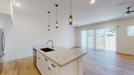 This two-story home showcases a clean, contemporary design with a thoughtfully planned layout across both levels. The main living area is open-concept, with light hardwood flooring flowing seamlessly from the kitchen through to the living space. A built-in desk nook adds functional character to the main floor, while a ceiling fan and recessed lighting keep the space comfortable and well-lit. Large sliding glass doors invite natural light and provide outdoor access.

The kitchen is a standout feature, centered around a generous island with a granite countertop, undermount sink, and seating potential. White shaker cabinetry with matte black hardware lines the perimeter, complemented by a striking chevron-patterned tile backsplash and stainless steel appliances. Three cylindrical pendant lights hang above the island, adding modern visual interest.

A compact powder room on the main floor features light hardwood flooring and a wall-mounted sink with a round mirror. Upstairs, carpeted bedrooms offer a quiet retreat, each with natural light from blinded windows and ceiling fans. Bathrooms include a full bath with a tub-shower combo and a primary bath featuring a frameless glass walk-in shower adorned with herringbone tile, adding an elevated, spa-like quality to the space.