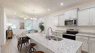 This single-floor home offers a thoughtfully designed open-concept layout that seamlessly connects the kitchen, dining, and living areas. The kitchen is a standout feature, boasting an expansive granite-topped island with an undermount stainless steel sink and bar seating, complemented by white shaker-style cabinetry, granite countertops, and a full suite of stainless steel appliances including a range, over-the-range microwave, and French door refrigerator. Light wood-look flooring runs throughout the main living areas, adding warmth and continuity to the space. The living area is bright and welcoming, illuminated by recessed lighting and a decorative chandelier, with windows allowing natural light to fill the room. The bedrooms are finished with plush carpet and generously sized windows fitted with blinds. The primary bathroom features a granite-topped vanity with white cabinetry, light wood-look flooring, and direct access to a walk-in closet. A secondary bathroom includes a clean, white tub-shower combination with brushed nickel fixtures. Throughout the home, a consistent neutral color palette, crisp white trim, and modern finishes create a cohesive, contemporary aesthetic.
