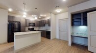 This single-story, two-bedroom, two-bathroom residence offers a thoughtfully designed open-concept layout. The kitchen serves as a central focal point, featuring dark espresso cabinetry, granite countertop surfaces, a tile backsplash, and a generous center island with additional storage. Black appliances, pendant lighting, and track lighting complete the space. Wood-look flooring extends throughout the kitchen and main living area, lending a warm, cohesive feel.

The living area is spacious and open, with a ceiling fan and easy access to the adjacent rooms. Both bedrooms are carpeted and receive natural light through multiple windows fitted with blinds. The primary bedroom connects directly to its en-suite bathroom, which includes a granite-topped vanity with dark cabinetry, a glass-enclosed shower, and tile flooring. A large walk-in closet with built-in shelving and hanging rods provides generous storage. The second bathroom offers a tub-shower combination with tile surround, a matching vanity, and tile floors. A built-in shelving nook near the entryway adds additional functional storage to the overall layout.