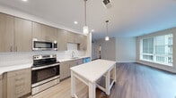 This well-designed 2-bedroom, 2-bathroom residence offers a functional and modern layout across a single floor. The kitchen is a standout feature, showcasing light wood-grain cabinetry, white subway tile backsplash, stainless steel appliances including a refrigerator, range, and built-in microwave, along with white quartz countertops and a center island. Pendant lighting adds a contemporary touch overhead, while wood-look flooring flows seamlessly throughout the space. The open layout connects the kitchen to the living room, which is bright and airy, featuring large windows fitted with blinds and direct access to a private balcony overlooking the exterior. The primary bedroom is generously sized, complete with its own closet and access to a dedicated bathroom. The second bedroom also benefits from natural light through a large window. Both bathrooms are finished with clean, modern fixtures; one features a full soaking tub and shower combination with white tile surround. Two closets provide ample storage throughout the residence. Neutral wall tones and consistent hardwood-style flooring unify the space, creating a cohesive, contemporary ambiance throughout.