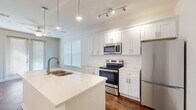 This efficiently designed one-bedroom, one-bathroom residence in Memphis, Tennessee offers a thoughtful layout with modern finishes throughout. The kitchen is a standout feature, showcasing crisp white shaker cabinetry extending to the ceiling, a quartz waterfall island with an undermount sink, and a full suite of stainless steel appliances including a range, over-the-range microwave, and refrigerator. Rich, dark hardwood flooring runs throughout the kitchen and main living areas, complemented by pendant lighting and a track lighting system that brightens the space. The bedroom offers a comfortable, carpeted retreat filled with natural light from a large double window dressed with blinds. A walk-in closet provides generous storage, and the room connects conveniently to the hallway. The bathroom is finished with classic white subway tile in the tub-shower surround, a white vanity with brushed nickel fixtures, a large mirror, and the same warm hardwood flooring carried throughout the home. Clean white walls and neutral tones create a bright, cohesive aesthetic across all rooms, making this Memphis residence a polished and practical living space.