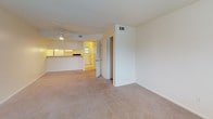 This two-floor residential space offers a practical and comfortable layout designed for everyday living. The open living area is finished with plush wall-to-wall carpeting and features a ceiling fan with integrated lighting, providing both comfort and airflow. A textured ceiling adds subtle character throughout the common areas. The living space flows seamlessly toward the kitchen, which is visible through a pass-through counter. The kitchen is efficiently laid out with ample white cabinetry, wood-toned laminate countertops, a double sink, a dishwasher, a full-size refrigerator, and a coil-burner electric range — all finished in white for a clean, cohesive look. Vinyl tile flooring completes the kitchen's functional design. The bedrooms are generously proportioned, each featuring soft carpeted floors, ceiling fans with light kits, and windows fitted with horizontal blinds that allow natural light to filter in while maintaining privacy. The bathroom includes a full-size soaking tub with a tiled surround and built-in shelving for added convenience. Throughout the space, a neutral color palette of whites and warm beiges creates a bright, clean atmosphere that is easy to personalize.