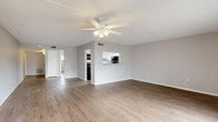 Located along N Tamiami Trail in Sarasota, Florida, this one-bedroom, one-bathroom residence offers a thoughtfully organized single-floor layout. The entryway hallway, illuminated by wall sconces, leads directly into the open living area, which is finished with warm wood-look flooring and a textured ceiling. A ceiling fan with integrated lighting serves as a central fixture, while large sliding glass doors flood the space with natural light and provide access to an outdoor balcony, offering views of the surrounding landscape.

The kitchen is accessible via a pass-through window from the living area and is equipped with cabinetry and appliances, maintaining a clean and functional design. Neutral gray walls throughout create a cohesive, understated aesthetic.

The bedroom features its own ceiling fan, wood-look flooring, and a horizontal window that brings in natural light while maintaining privacy. A sliding door panel provides closet access, keeping the room practical and uncluttered.

The bathroom is well-appointed with a tiled tub-and-shower surround, a white vanity with granite countertop, a framed mirror, and wood-look tile flooring. A frosted window above the tub adds natural light without sacrificing privacy. The overall ambiance is clean, bright, and move-in ready.
