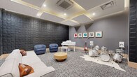 This 2,240 square foot single-floor space located at 634 Newark Ave, Jersey City, NJ, is a meticulously designed communal area that seamlessly blends functionality with style. The open-plan layout is characterized by its modern aesthetic, featuring light wood flooring and a sophisticated neutral color palette. 

The space is divided into distinct zones, each serving a specific purpose. A prominent game area includes a pool table and shuffleboard table, providing entertainment options for residents. Comfortable lounge spaces are scattered throughout, featuring plush sofas and armchairs in muted tones, perfect for relaxation or casual conversations.

The room's ambiance is enhanced by its thoughtful lighting design. Recessed ceiling lights are complemented by pendant lamps and indirect lighting, creating a warm and inviting atmosphere. Large windows allow ample natural light and offer views of the surrounding area.

A notable feature is the adjoining conference room, visible through glass partitions, which adds versatility to the space. Modern amenities include wall-mounted TVs and contemporary artwork, contributing to the overall upscale feel.

The attention to detail is evident in the textured wall treatments, including wood paneling and decorative wall coverings. This multifunctional space is designed to foster community interaction while providing areas for both active recreation and quiet relaxation.
